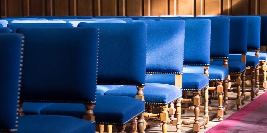 A courtroom with wooden paneling, a red carpet, and rows of blue chairs.