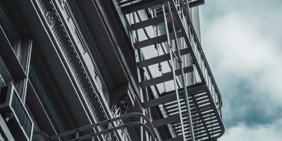 A metal fire escape with several landings connected by stairs, on the side of a old building, with ornate details on the facade.