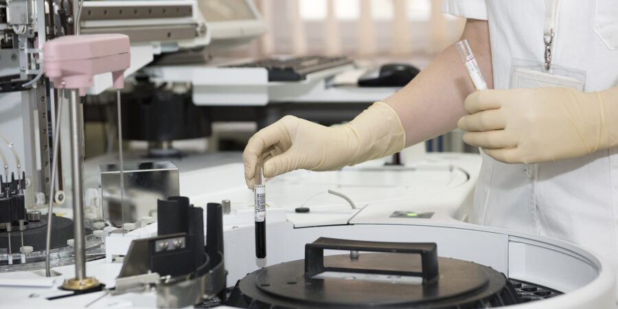 A lab technician switching test tubes with liquid in and out of a machine that spins to mix the contents of the test tubes.