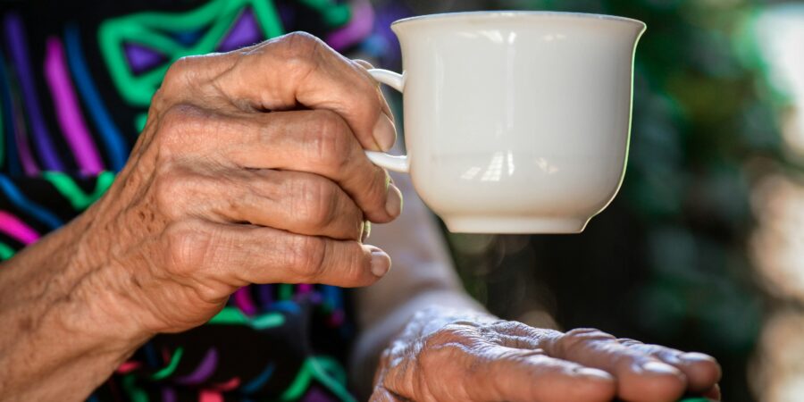 A close-up of an older woman's hands, holding a small coffee cup.