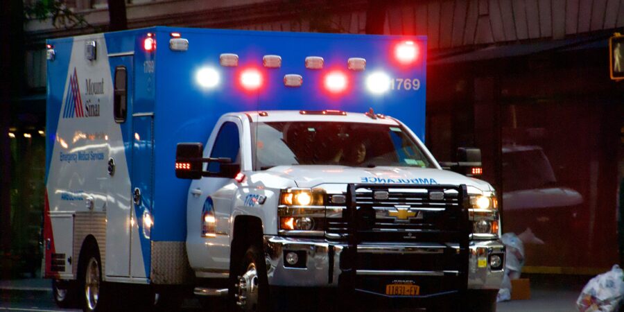 A blue and white ambulance with flashing lights driving through a city at night.