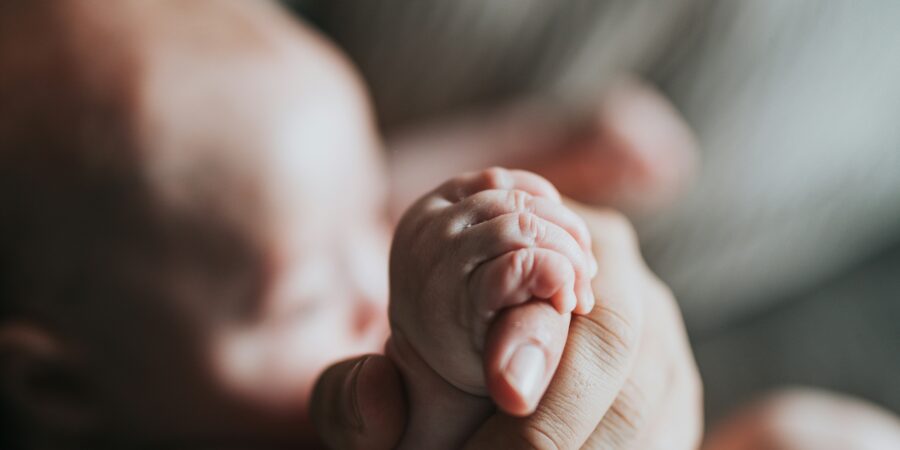 A close-up of someone holding a baby, with the focus on the small baby's hand holding. on to the adults hand.