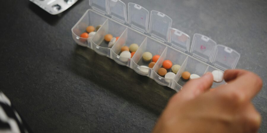 A close up view of someone taking a pill in or out of a pill container that has sections for each day of the week and the daily doses of pills in each section.