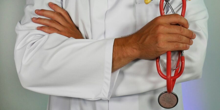 A close up view of a doctor with his arms crossed and holding a red stethoscope in one hand.